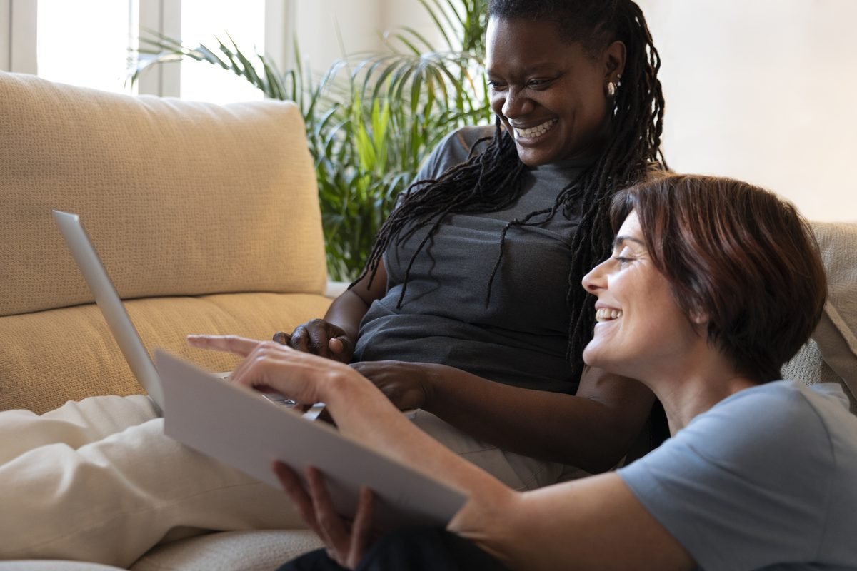 A support worker and a client sitting together at home, looking at a laptop