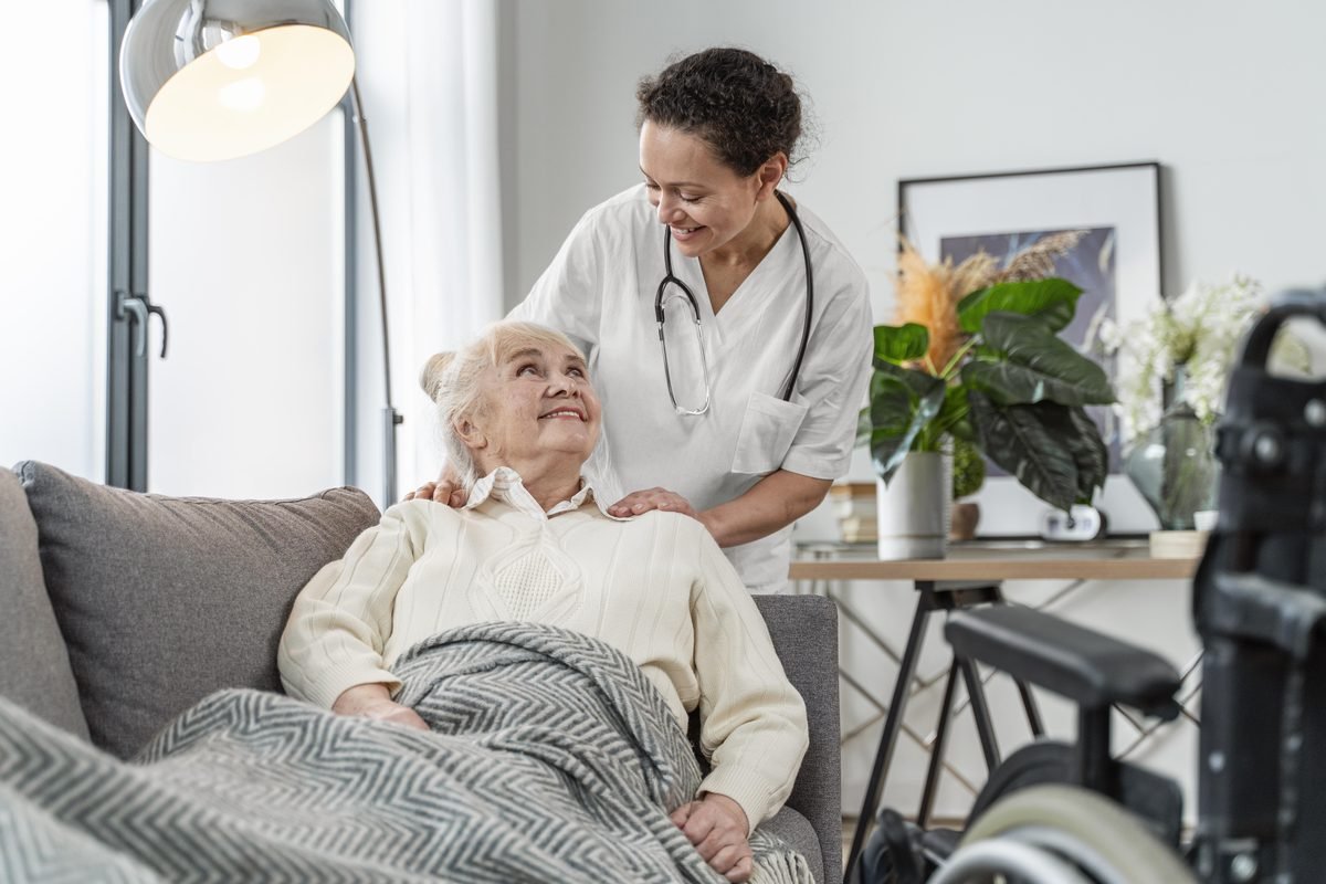 A care worker checking in on an elderly client resting on her sofa at home
